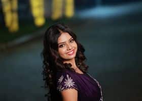 Charming woman with dark hair wearing a purple dress smiling outdoors at night.